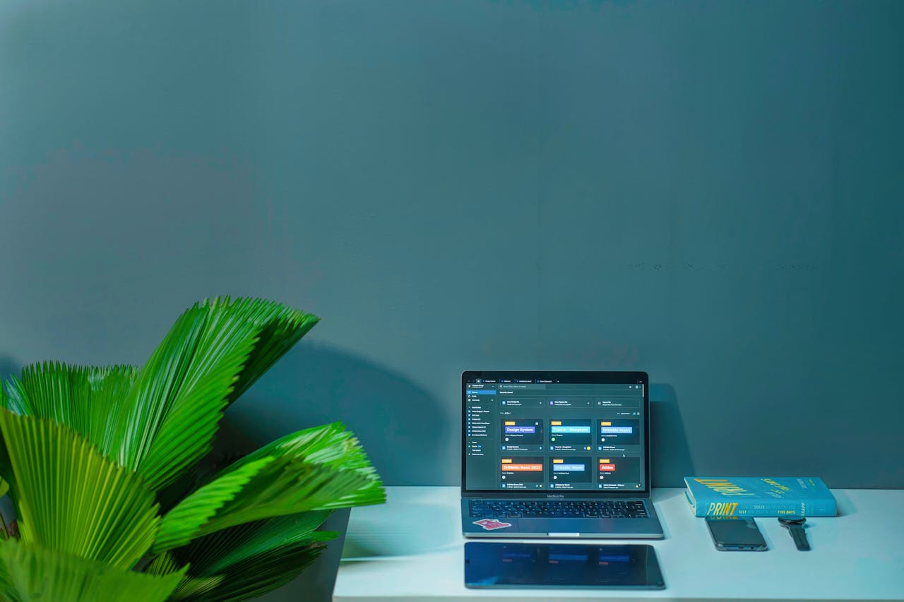 Sleek office desk setup featuring a laptop, tropical plant, and book in a modern design.